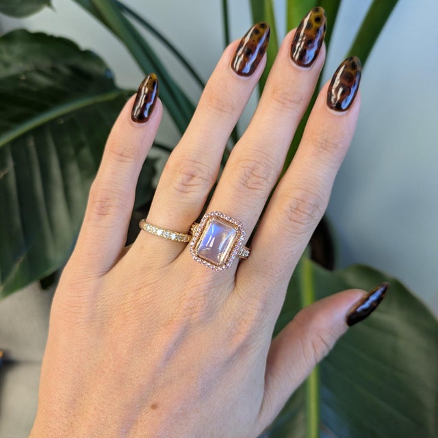 A 5.93-carat rainbow moonstone cabochon glows with a floating blue adularescence at the centre of this solid 14K rose gold...
