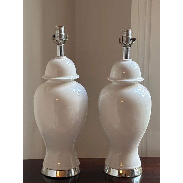 An elegant pair of circa 1960s ceramic ginger jar table lamps in a soft white, glossy glaze and chrome accents. These...