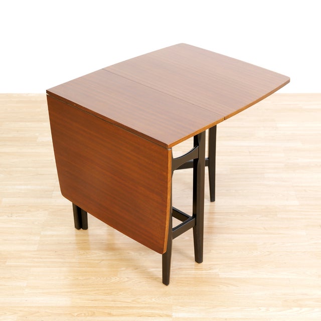 This mid-century drop leaf dining table was produced by in England during the 1960s. With an ebonzied frame and Mahogany...