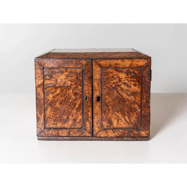 Small Regency tabletop cabinet. Two doors fronting three drawers. Figured walnut, brass inlay, and ring handles. England...