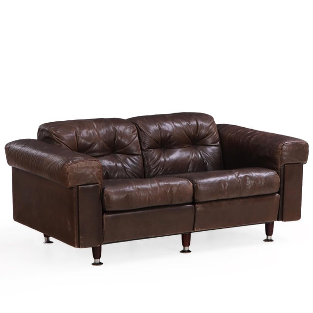 Swiss modern leather loveseat, circa 1970s, in the style of De Sede. Features rich brown leather upholstery with a tufted...