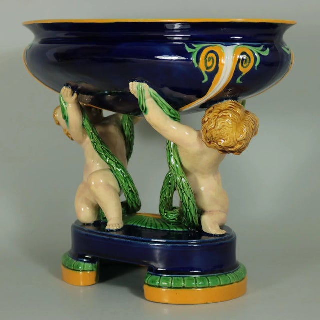 Minton Majolica figural bowl which features putti holding leafy garlands, supporting the bowl. Colouration: cobalt blue,...