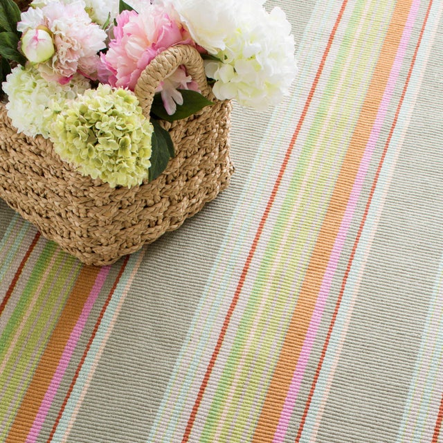 Bright stripes of red, orange, pink, citrus, and sky pop against sage green on this eco-friendly indoor/outdoor rug made...