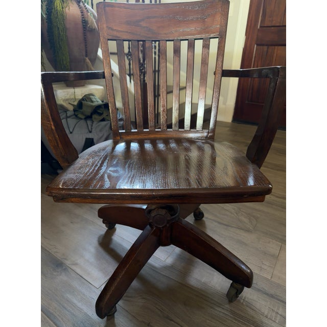 Solid oak vintage office/desk armchair featuring a slat back, contoured wood seat, armrests, four-leg caster base, and...