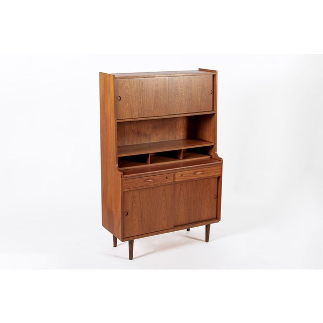 This vintage mid century Danish modern tall teak wood bookcase cabinet and secretary desk was made in Denmark circa 1960....