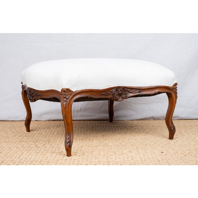 An upholstered ottoman or footstool, c. 1900, French. Louis XV style and featuring carved floral and shell motifs. The two...
