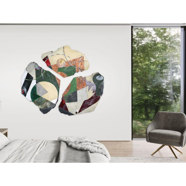 Three irregular ceramic slabs arranged together as a single wall piece, each carrying a different but related surface....
