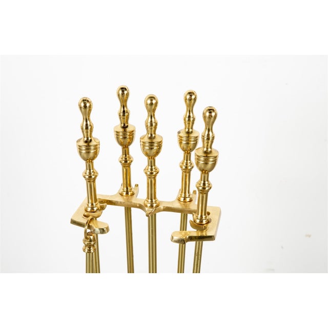 A brass five piece tool fireplace set with a rectangular footed base with an arched brass carrying loop and a brass...