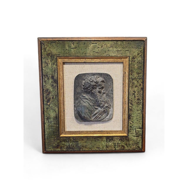 Decorative bronze relief plaque depicting a stylized human face, presented within an elegant frame. The sculpture is...