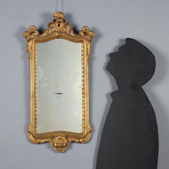 Small gilded wooden mirror carved with leaves and scrolls, with a shell at the base. Italy, 20th century. This piece is...