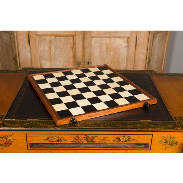 An English satinwood desk and game table from the 19th century with tilt top writing area, checkerboard and two drawers....