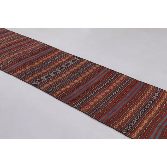 Made with handwoven wool circa 1950-1960, this 3x12 vintage Kilim enjoys dense horizontal band and intricate geometric...