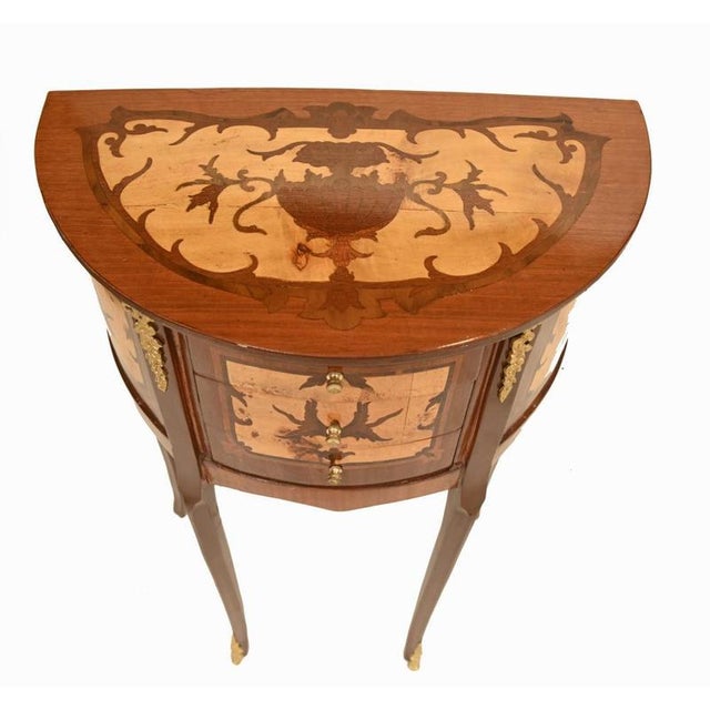 A highly elegant pair of french demi-lune bedside cabinets in the louis xvi style crafted in kingwood and richly decorated...