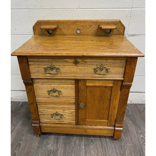 This is an antique late Victorian Eastlake-style washstand or commode in golden oak, dating to approximately 1890–1910. It...