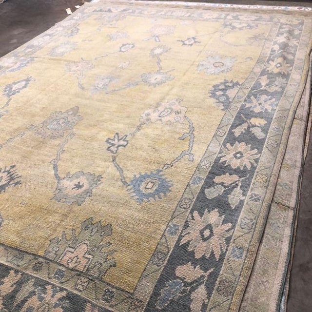 A contemporary hand-knotted Turkish Oushak rug featuring a warm golden beige field accented by large-scale floral motifs...