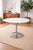 A sleek mid-century tulip-style dining table featuring a minimalist round top and sculptural chrome pedestal base....