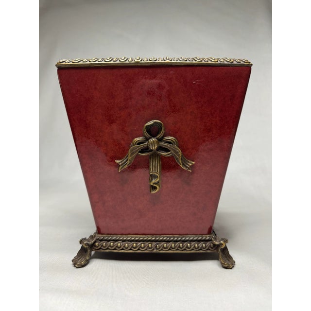 A beautiful rich, mottled ruby and crimson red to cinnabar color adorns the ceramic and brass jardiniere. The piece is in...