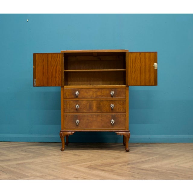 An elegant mid-20th-century tallboy cabinet, dating to the late 1940s–early 1950s, finished in warm burr walnut veneer....