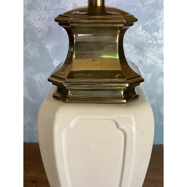 An American Stiffel table lamp from the 1950s, featuring a cream-colored ceramic body mounted on a stepped brass base. Its...