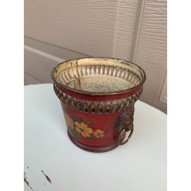 A gorgeous neoclassical red & gold tole cachepot, planter, or vase with head-painted floral details and brass lion heads...