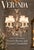 This elaborate multi-light chandelier features a central fluted glass column adorned with brass scrolling arms and draped...