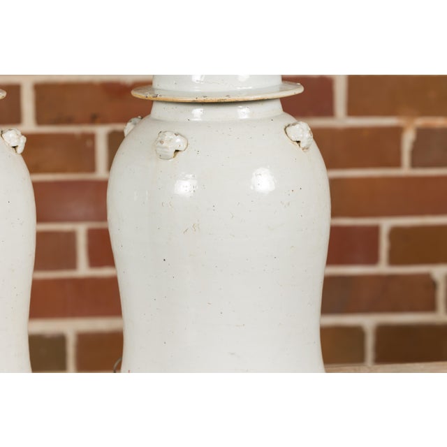 A pair of white porcelain lidded urns made into table lamps with single lights on circular gilded bases. Immerse your home...