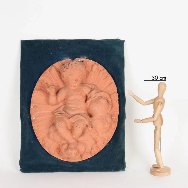 Patinated plaster sculpture depicting the blessing Infant Jesus mounted on a wooden panel covered in non-coeval velvet....