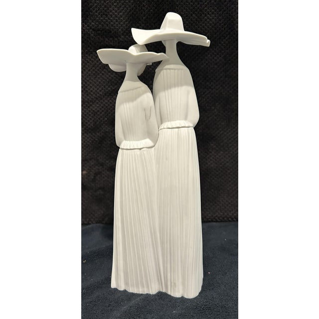 This porcelain figurine is the Lladró "Nuns" (model 4611), featuring two nuns with ribbed white habits and delicate rosary...
