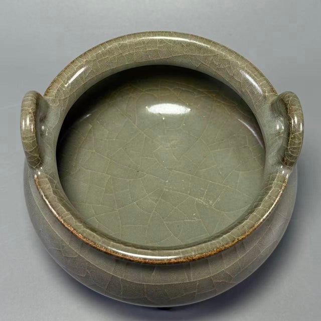 A graceful Chinese celadon tripod vessel, crafted with elegant upward‑curving twin side handles. Rounded bulbous body...
