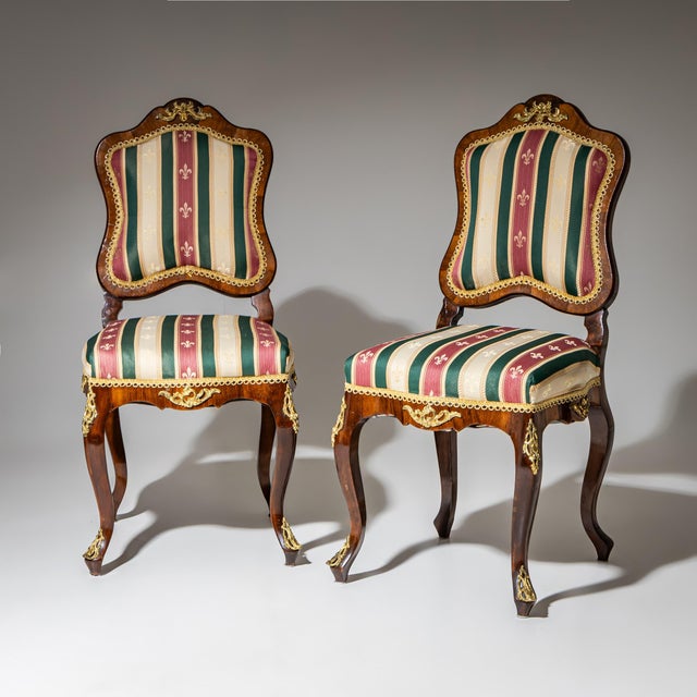 Pair of walnut chairs featuring gilded Rococo appliqués, a serpentine frame, and gracefully curved backs.