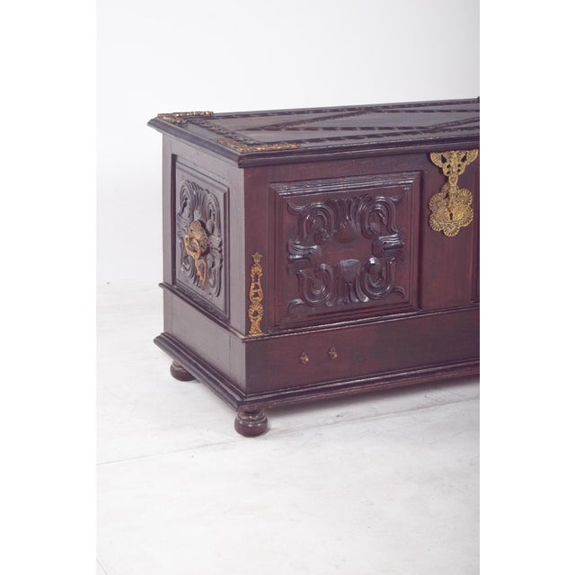 Carved wooden chest with gilded fittings. The top is richly carved with geometric details framing the surface and...
