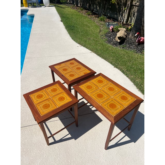 Set of three stamped Toften Denmark teak and tile nesting tables. The den has mustard yellow and orange abstract...