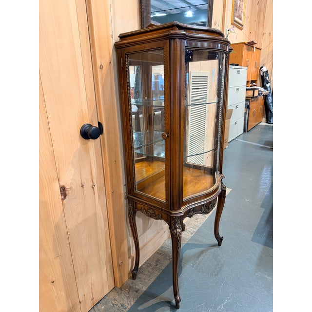 This is a graceful Louis XV style glass curio cabinet with softly curved lines and a warm, inviting wood finish. The...