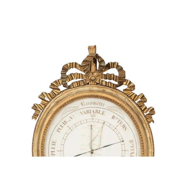 Louis XVI Giltwood Barometer By Toricelli. With carved ribbon and bow above an oval dial painted in creme and grisaille...