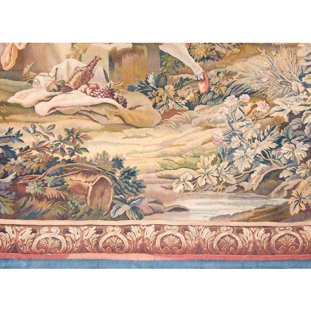 This antique French tapestry, dating to the early 20th century, depicts a classic pastoral scene with figures in a lush,...