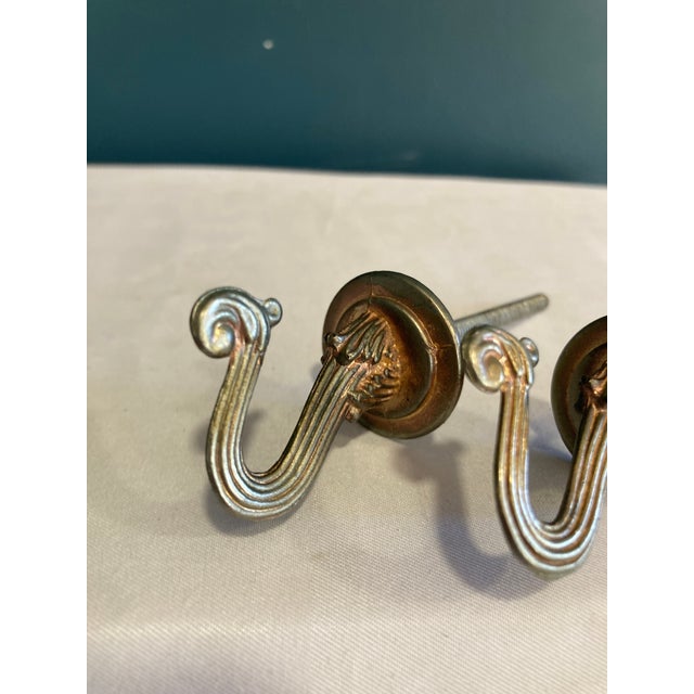 This pair of vintage brass drapery tieback hooks showcases a graceful scroll silhouette with fluted detailing and a rich...