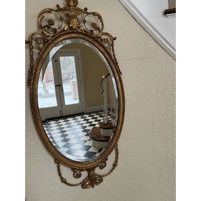 Exquisite gilt hand crafted mirror by Friedman Brothers. The mirror is oval with a beveled edge. This is an Adams styled...