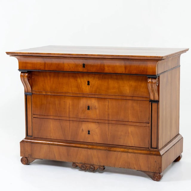 Biedermeier chest with volute legs, veneered in cherry with four drawers. The corpus with flanking volute capitals and...