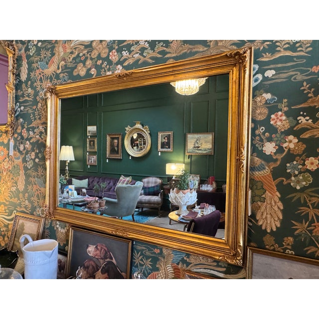 Rectangular, gold-gilded wall mirror with a classic frame featuring fluted inner edges and corner detailing, typical of...