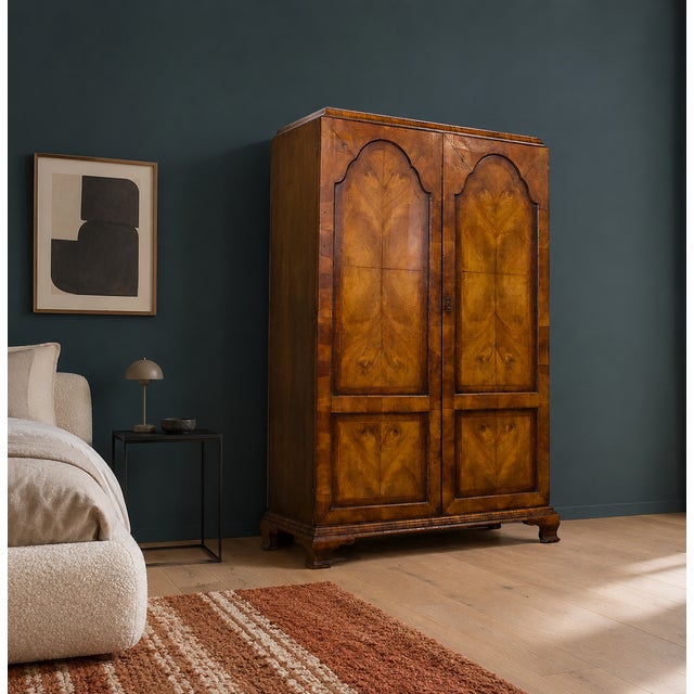 An early 20th-century double wardrobe featuring bookmatched figured walnut veneer, arched moulded door panels and shaped...