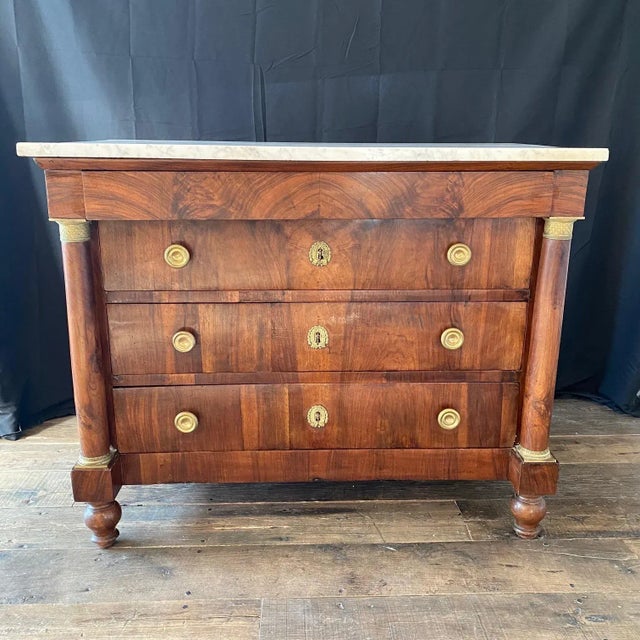 A French Neoclassical commode with marble top and exquisite brass accents. This antique chest features a rectangular-...