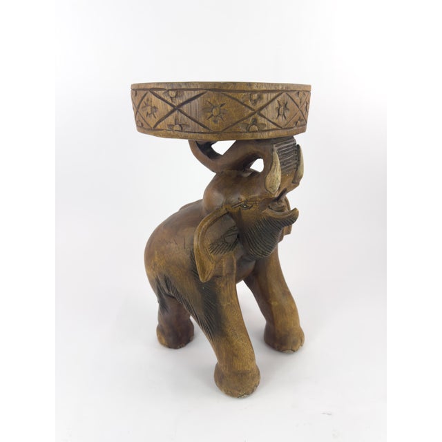 A charming vintage stool/side table carved from a single solid block of hardwood, depicting an elephant carrying a...