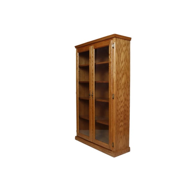 A traditional wooden bookcase made of oak with oak veneers. The solid oak frame supports four oak veneered shelves behind...