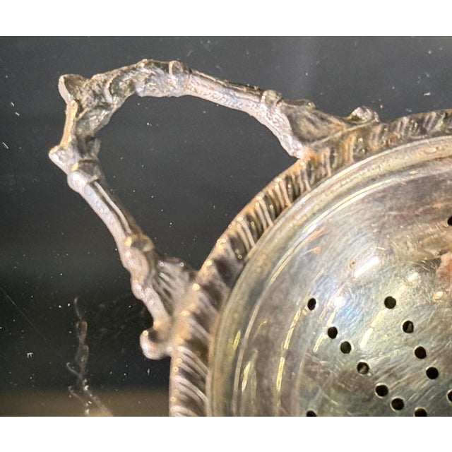 This English silverplate tea strainer is a nicely detailed example of the form, with a pierced bowl, feather-chased rim,...