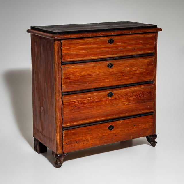 Narrow red-painted commode with four drawers, featuring a shaped upper drawer front and small baluster feet. The red...
