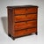 Narrow red-painted commode with four drawers, featuring a shaped upper drawer front and small baluster feet. The red...