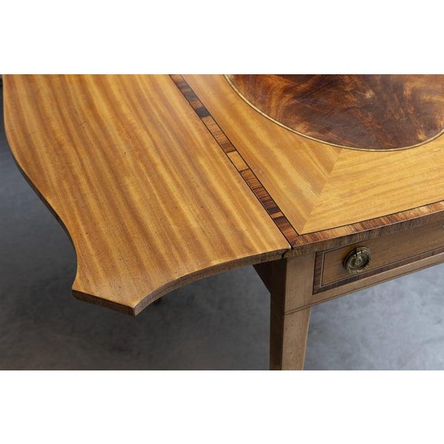 This is a fine George III English Pembroke table crafted in satinwood with richly figured mahogany crossbanding and...