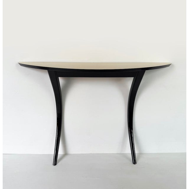 An elegant, designer entryway console table featuring clean, elegant lines. It features a half-moon top covered in fine...