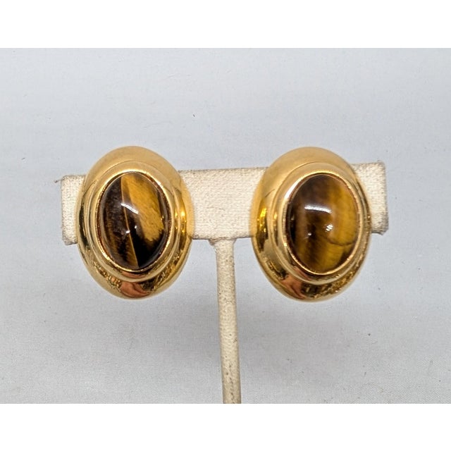 1980s oval goldtone cabochon faux-tiger's eye clip earrings. Marked "ALEXIS © KIRK" on the backs. Measure: 1 3/16 inches...