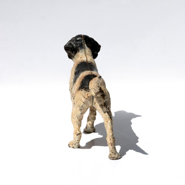 Painted cast iron figure of a hunting dog, modeled in a pointing stance, left foreleg raised and the feathered tail...